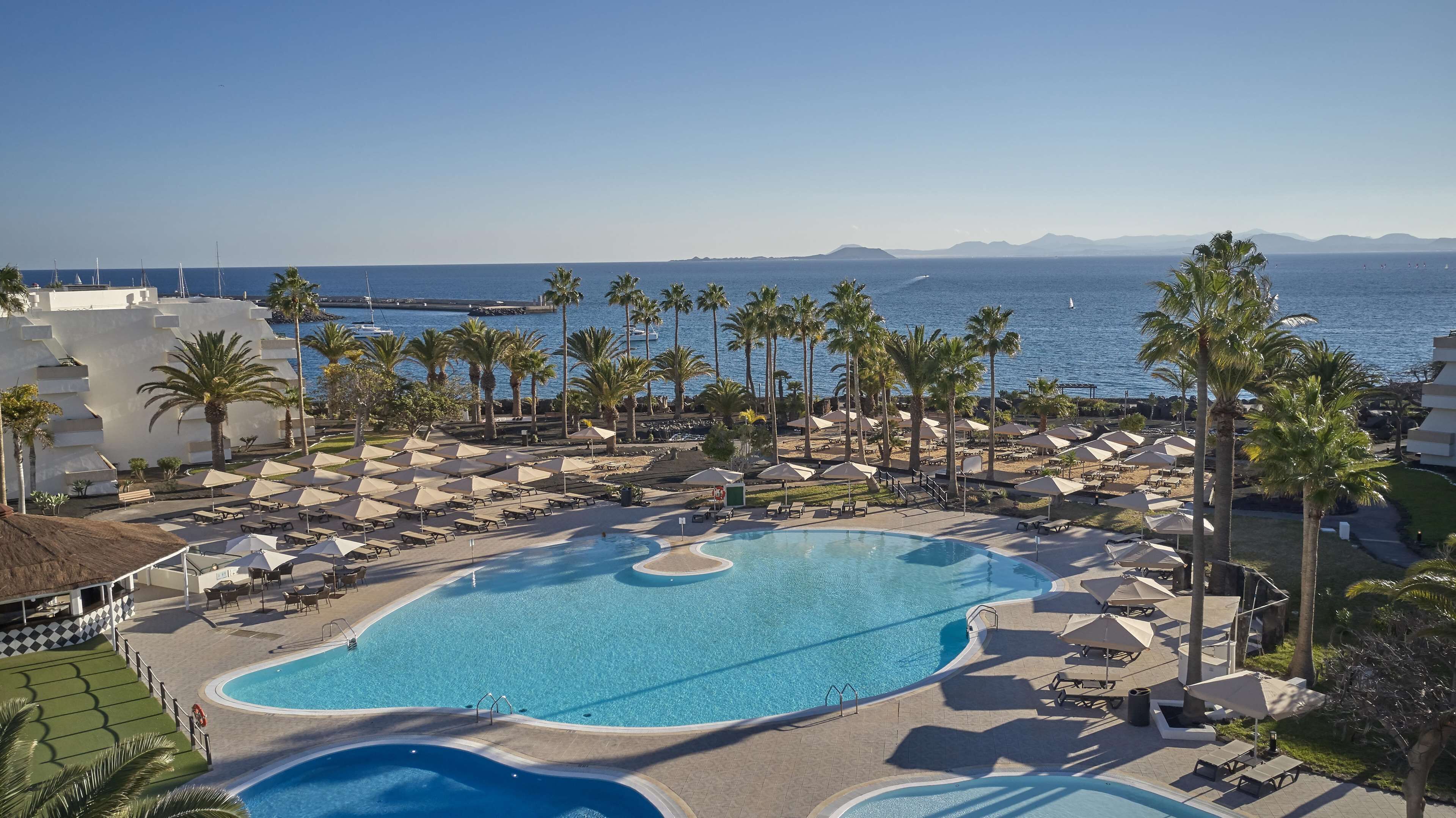 A resort with a large pool, sun loungers, umbrellas, and palm trees.