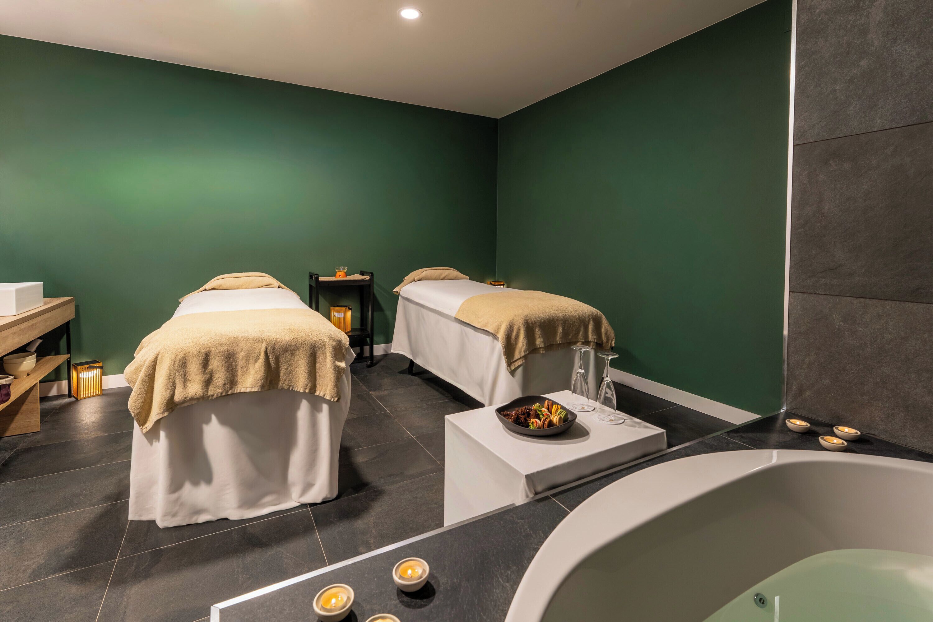 Un cuarto de spa con dos camas, una bañera y una mesita con velas.