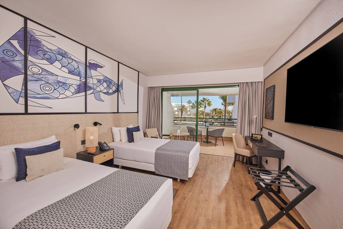 A hotel room with two beds, a desk, a TV, and a balcony with a view.