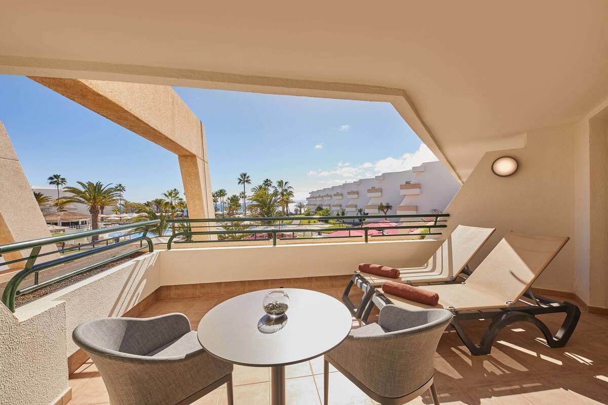 A balcony with a round table and two chairs, a pool, and a building in the background.