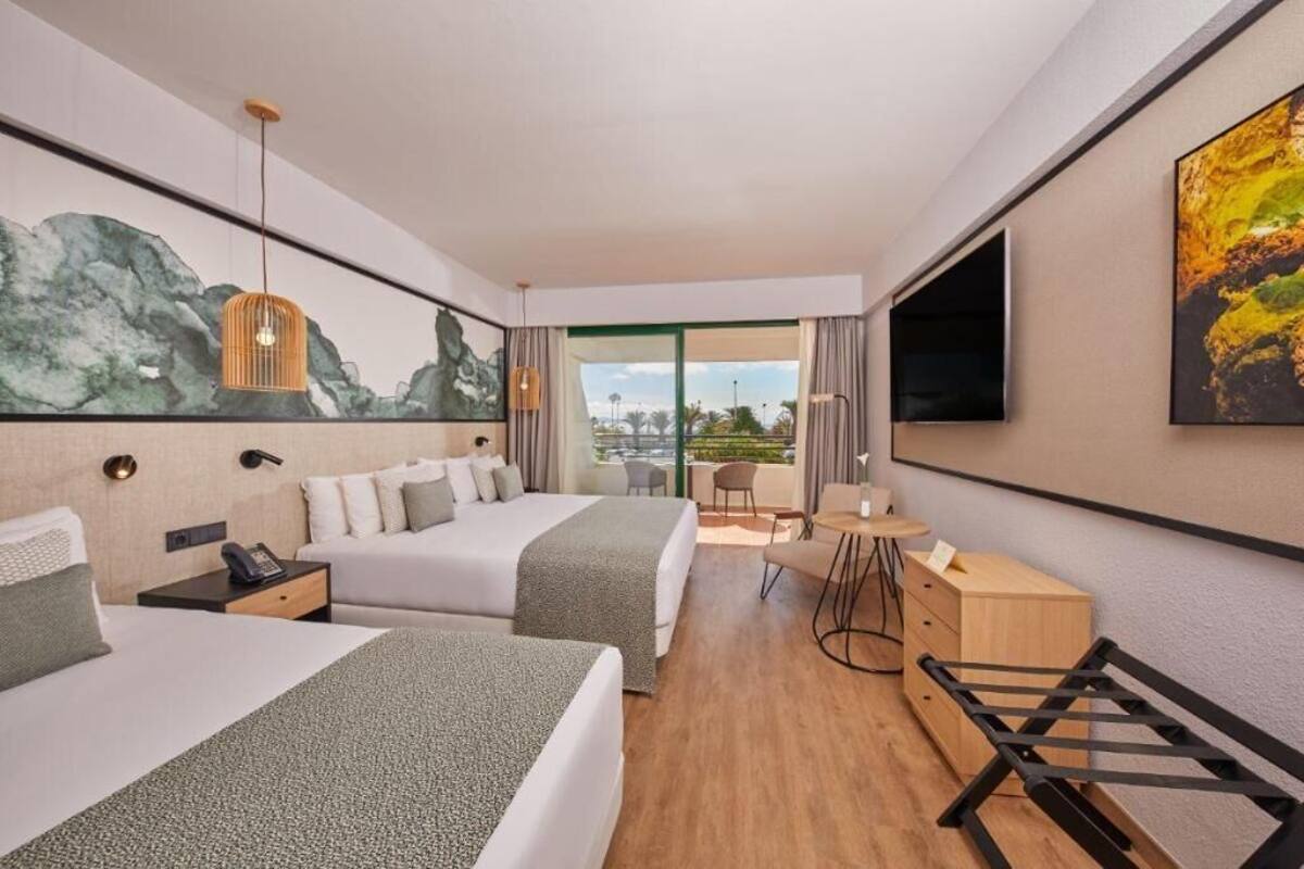 A hotel room with two beds, a desk, a chair, a TV, and a large window with a view.