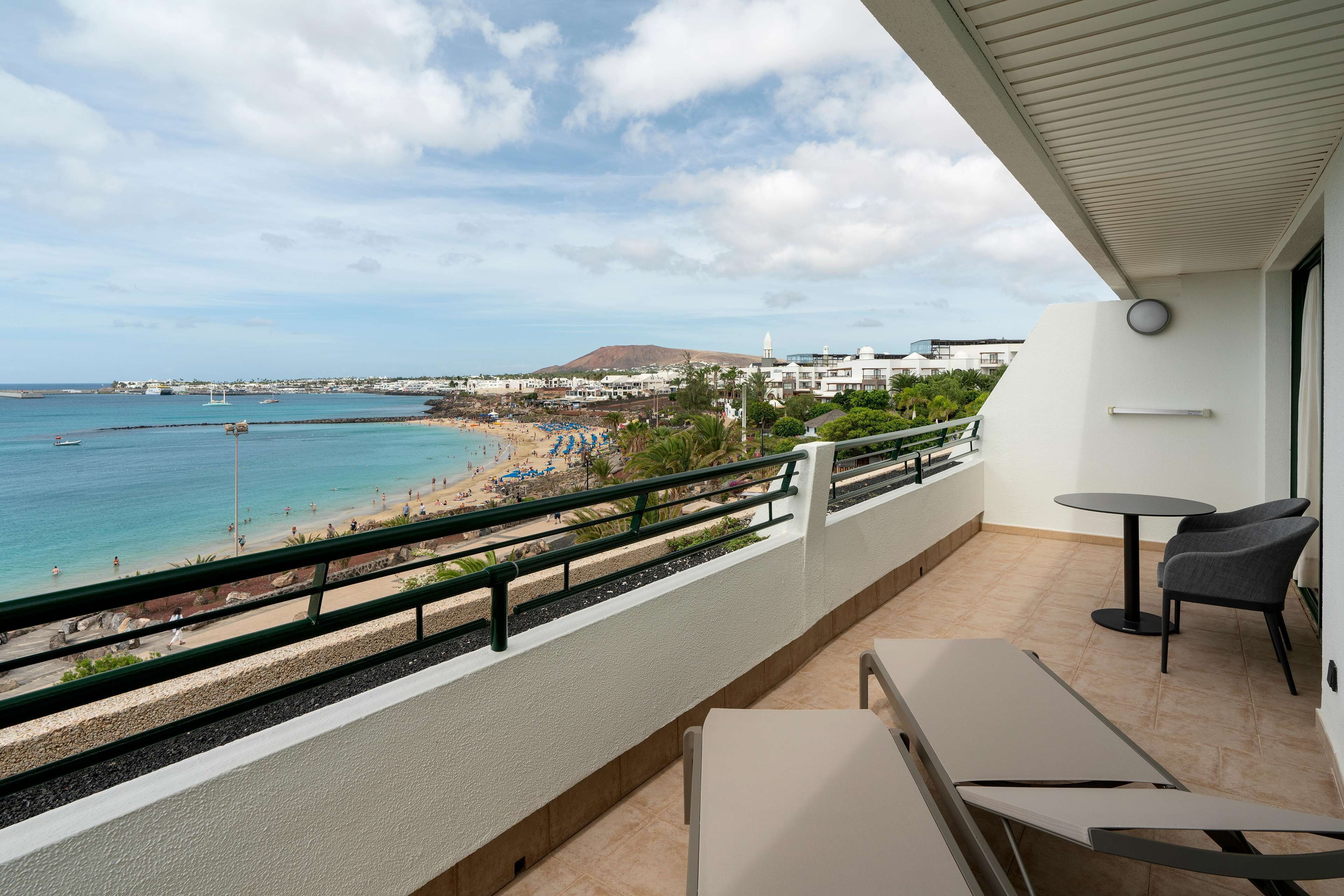 A balcony with a view of a beach, a table, and two chairs.