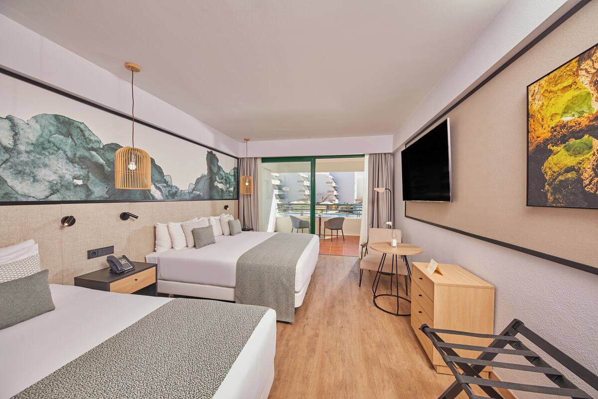 A modern hotel room with two beds, a desk, a chair, a TV, and a balcony with a view.