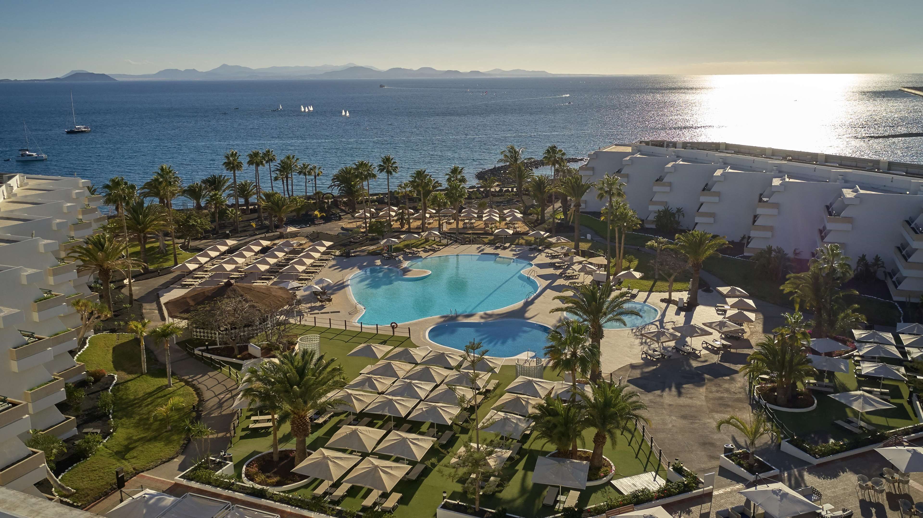 A resort with a large pool, palm trees, and a view of the sea.
