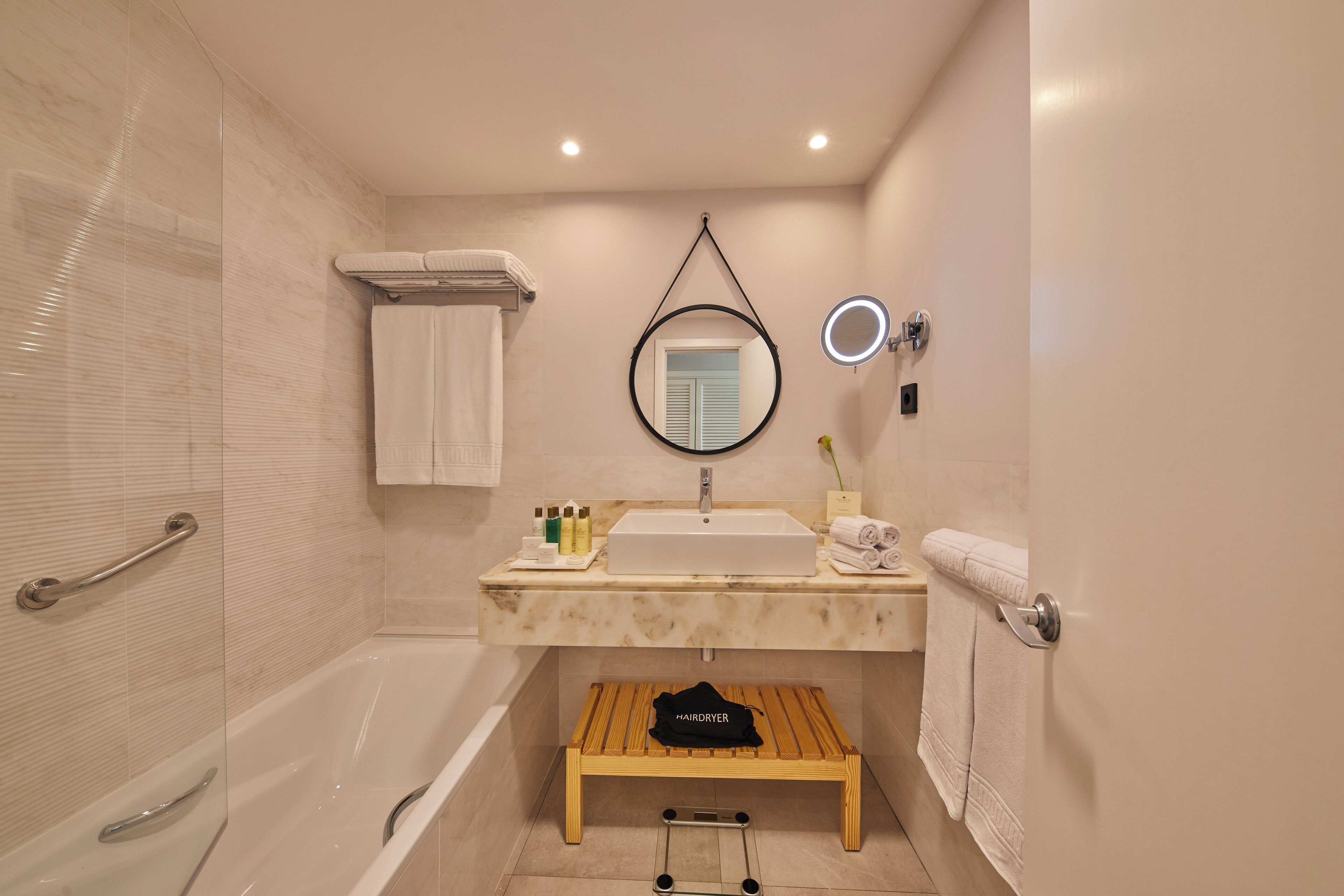 Un baño con bañera, lavamanos, espejo y toallero.