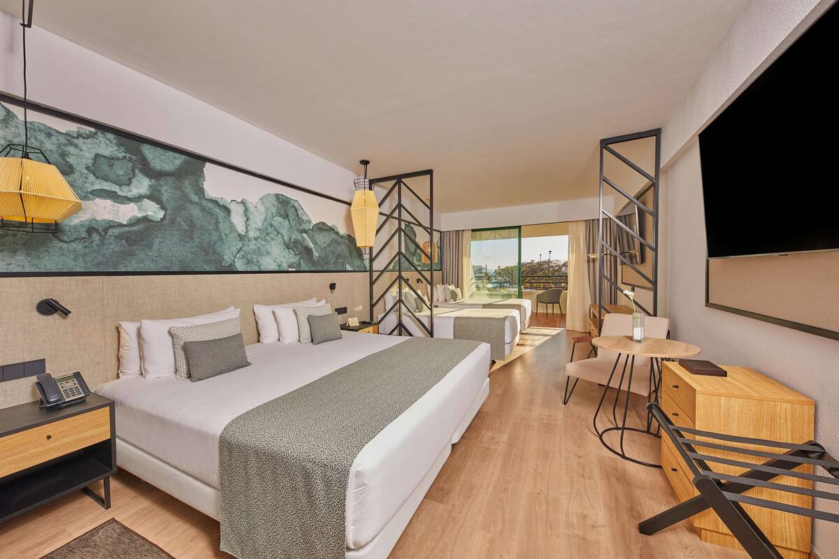 A hotel room with a large bed, two smaller beds, a desk, and a TV.