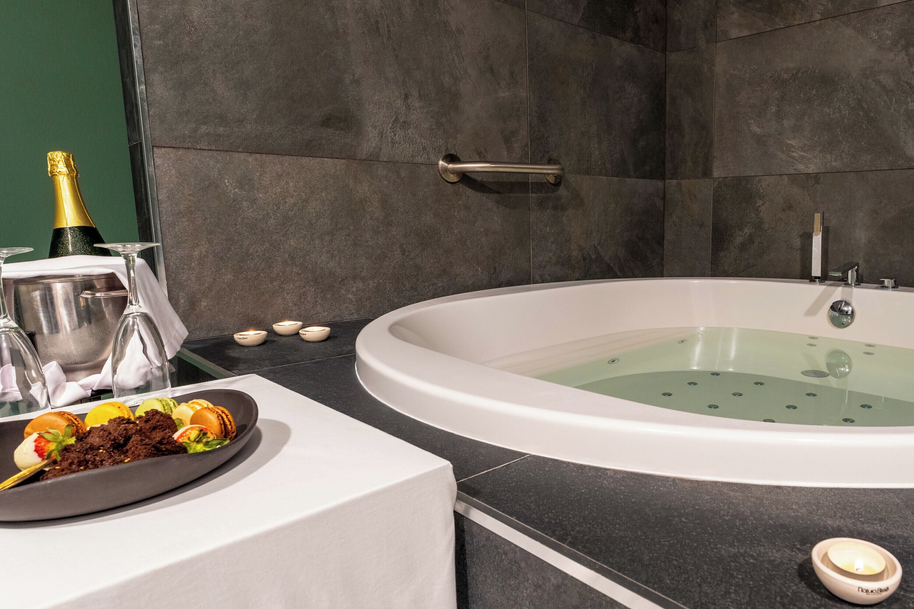 Une salle de bain moderne avec une baignoire, une coupe de champagne et une assiette de nourriture.