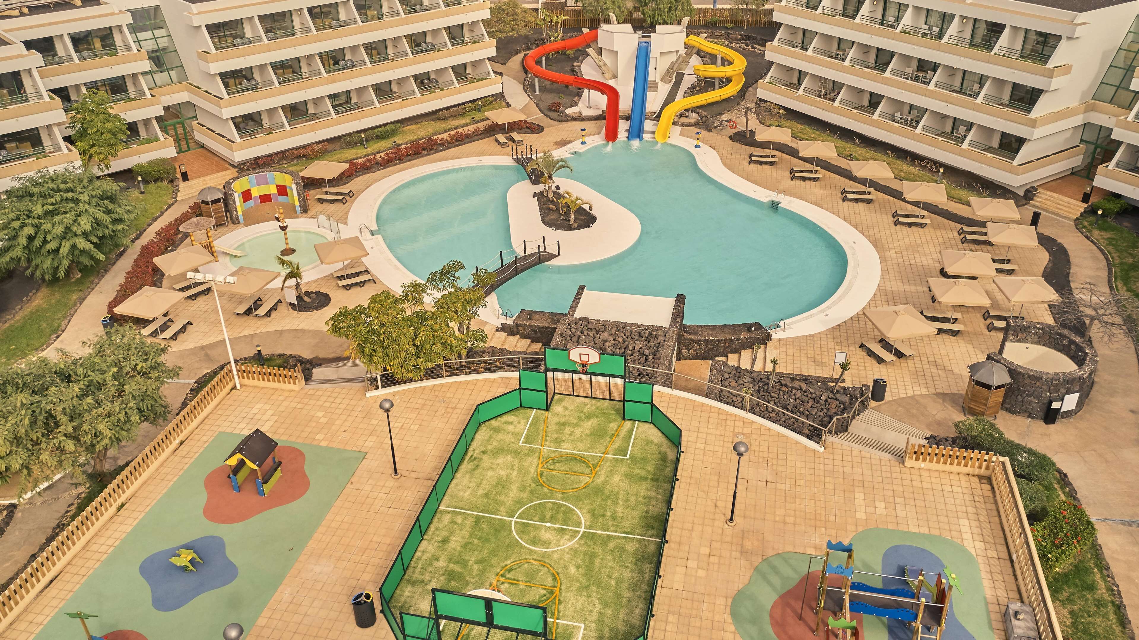 Un complexe hôtelier doté d’une piscine, d’un terrain de basketball et d’une aire de jeux.