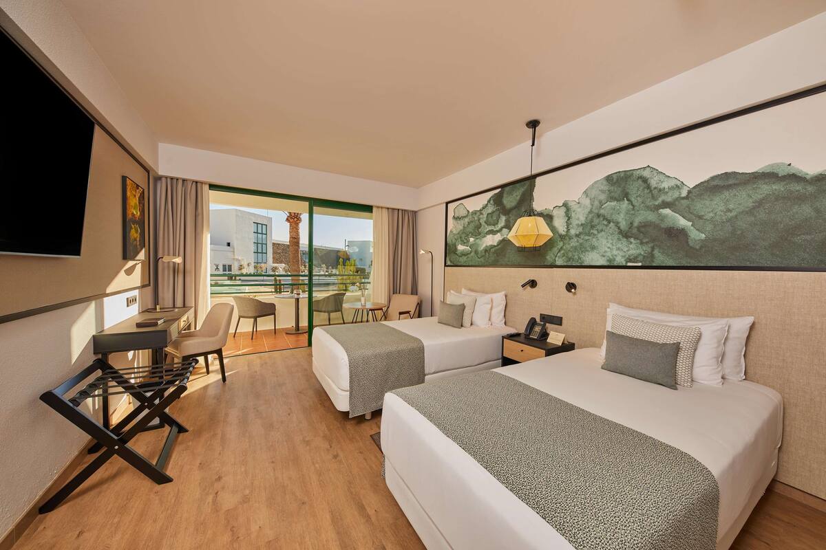 A hotel room with two beds, a desk, a chair, a TV, and a painting on the wall.