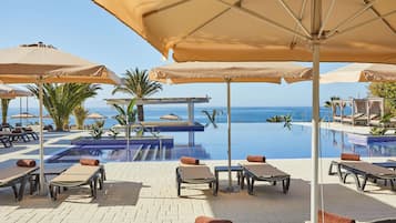 Zona de piscina con sillones de descanso y sombrillas, con vista a un mar azul y transparente.