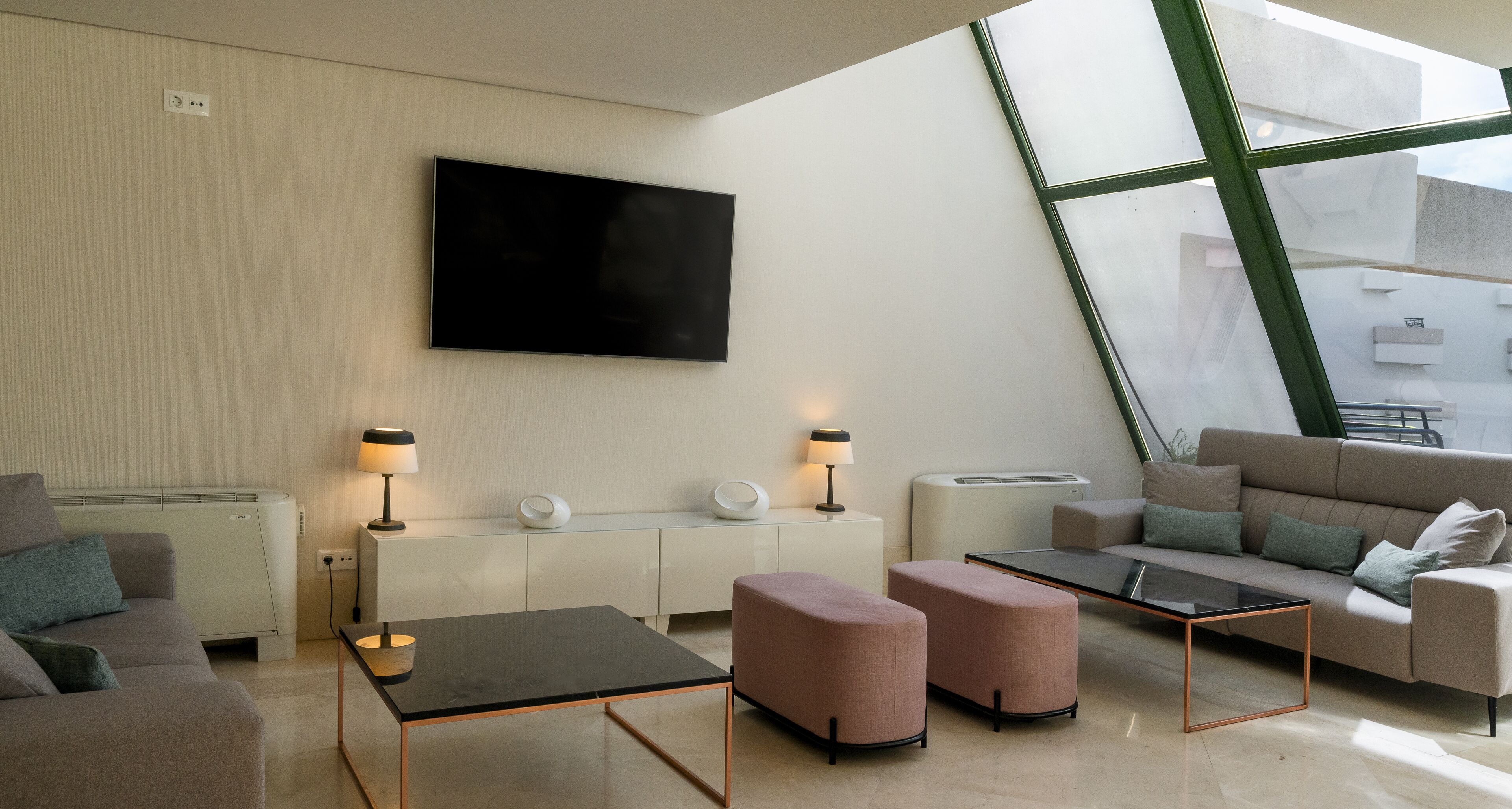 A modern living room with a flat-screen TV, two side tables with lamps, a sofa, and a glass coffee table.
