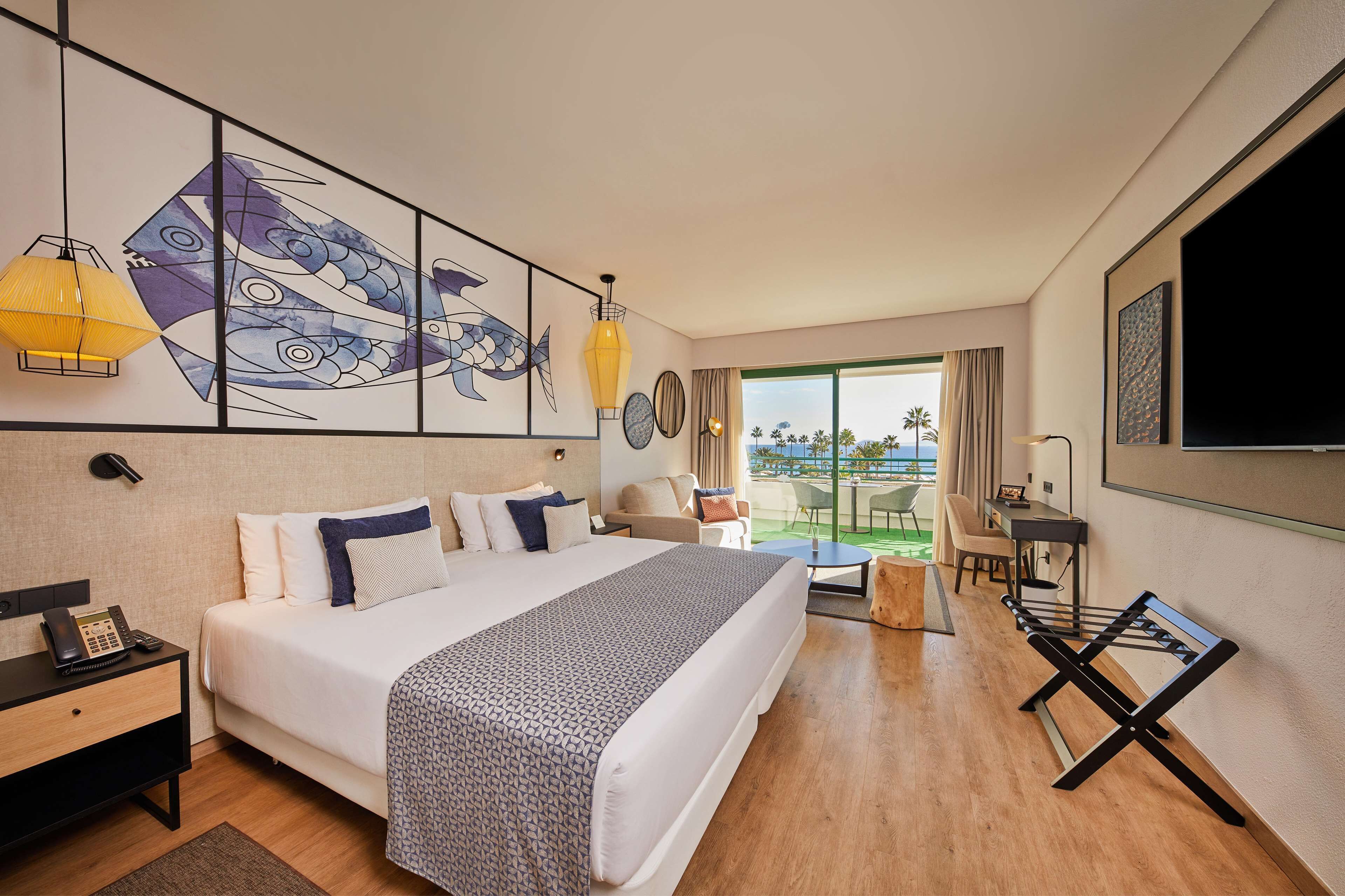 A modern hotel room with a large bed, a desk, a chair, and a view of the outdoors.