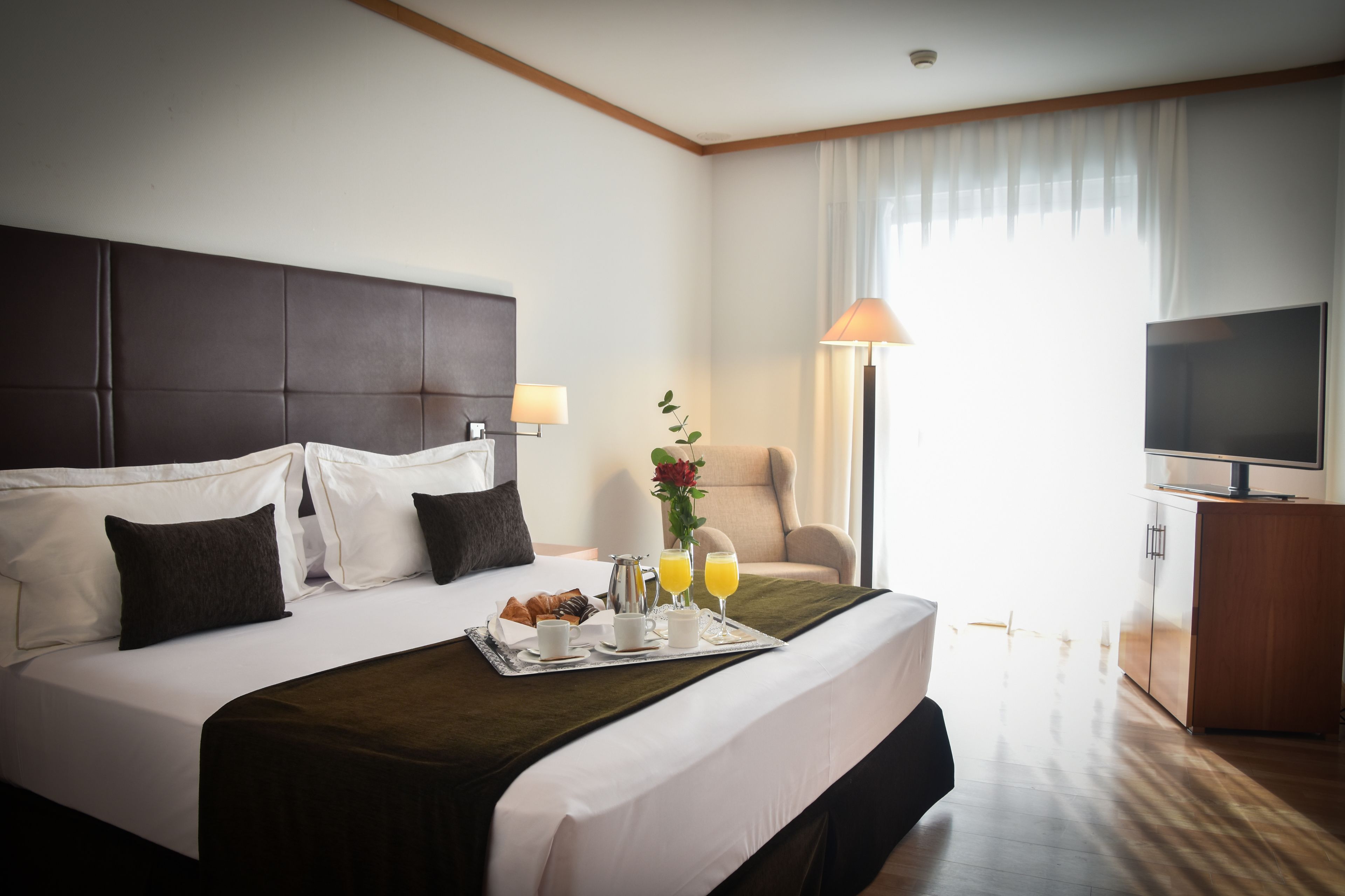 Habitación de hotel con una cama grande, un televisor de pantalla plana, un escritorio con lámpara y una ventana con cortinas.