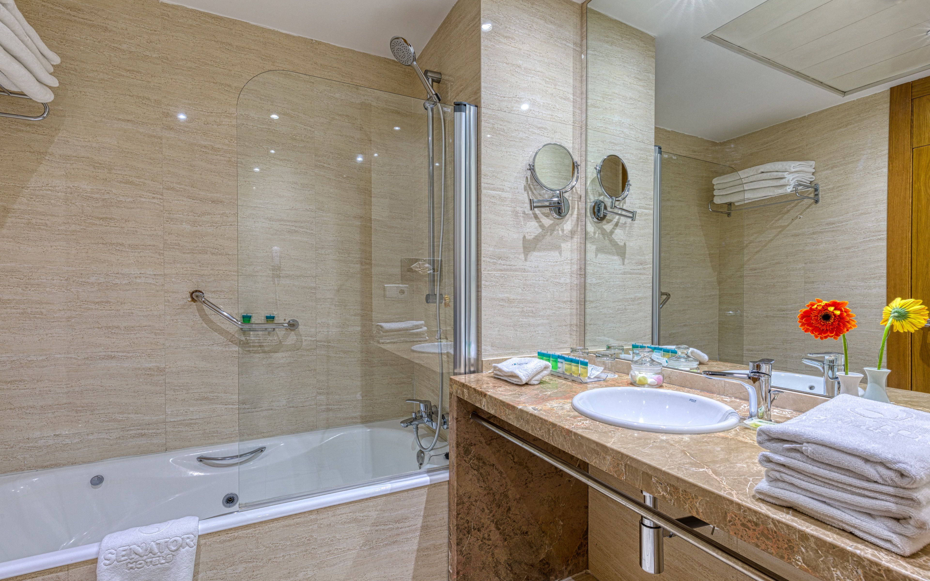 Un baño moderno con ducha envuelta en vidrio, lavamanos y tocador con toallas.