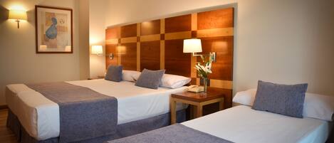 A hotel room with two beds, each with a grey bedspread and pillows, a wooden headboard, bedside lamps, and a framed artwork on the wall.
