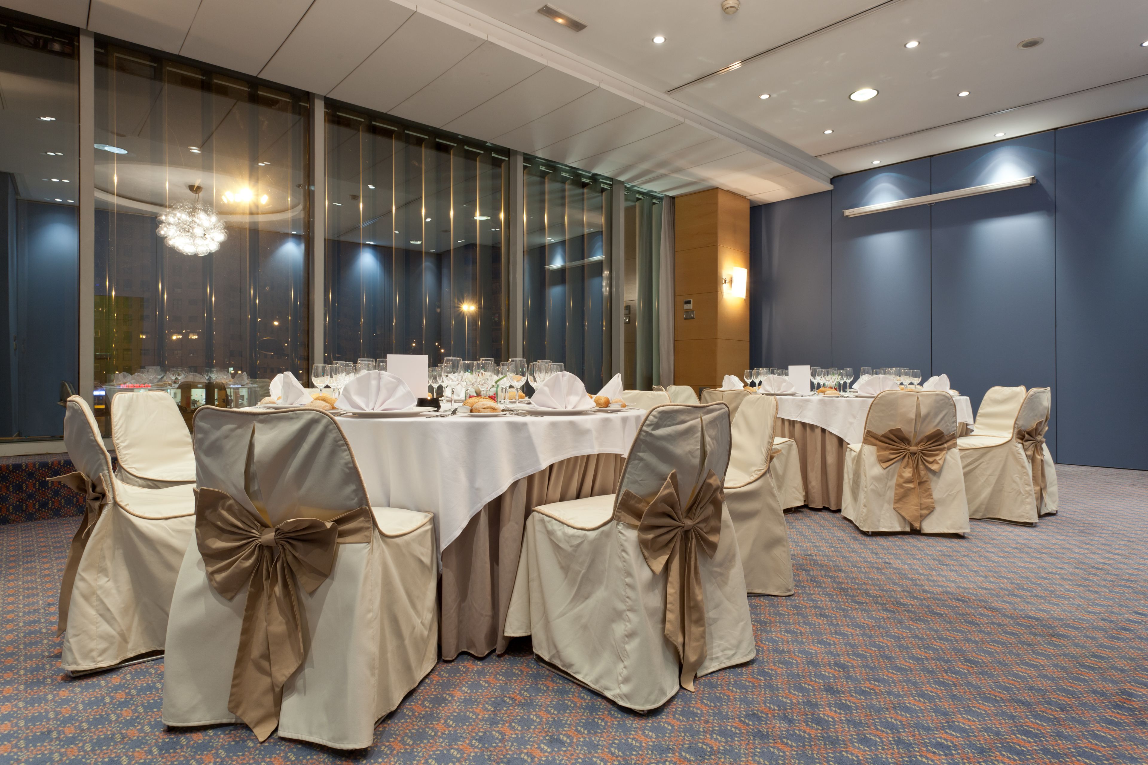 A banquet hall with round tables, chairs with bow sashes, and a patterned carpet.