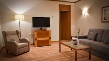 A living room with a sofa, armchair, TV, wooden cabinet, and a glass coffee table.