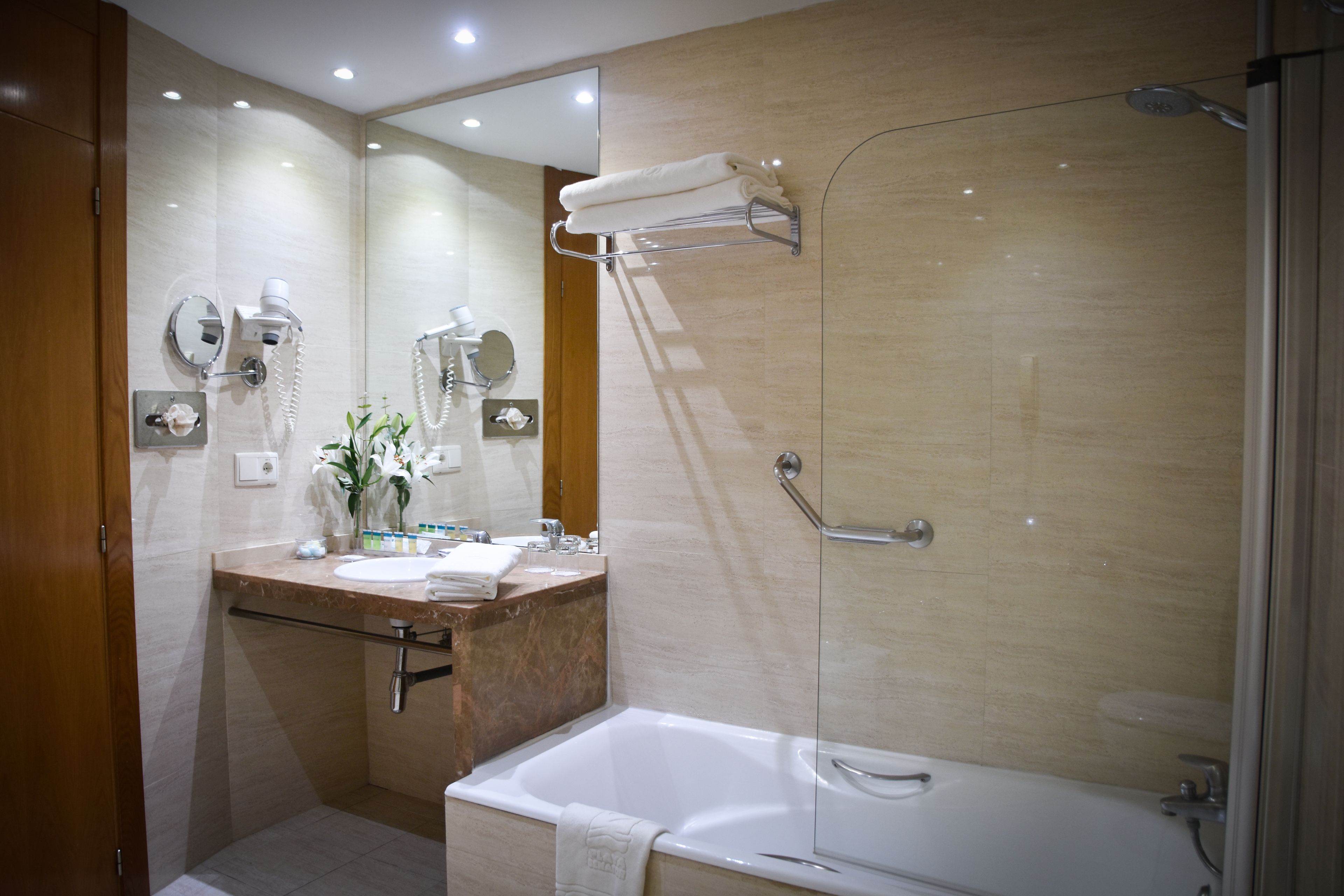 A modern bathroom with a large mirror, a sink, a bathtub, and a glass-enclosed shower.