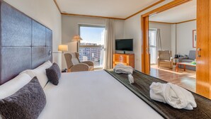 Ein Hotelzimmer mit einem großen Bett, einem Fernseher, einer Couch und Blick auf die Stadt.