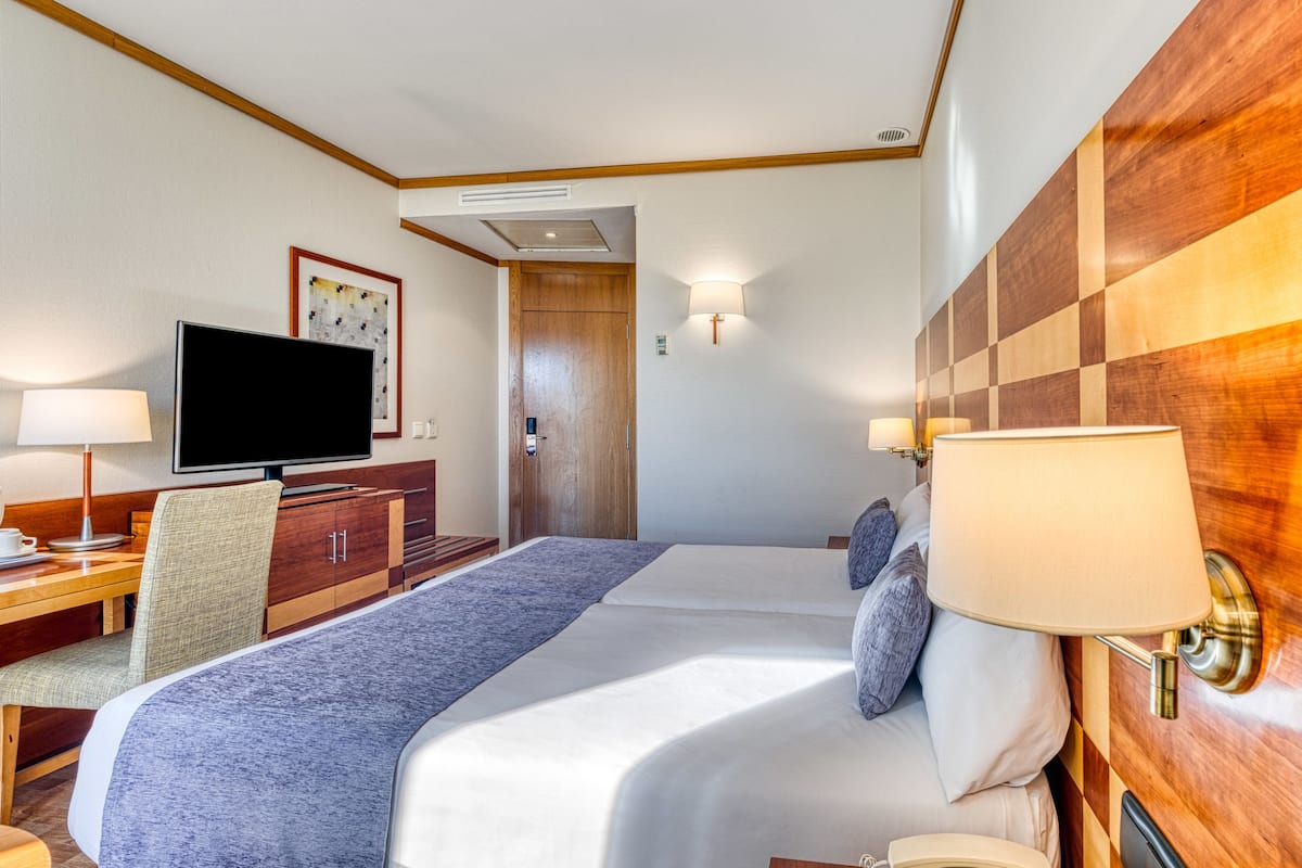Une chambre d’hôtel comprenant un lit, un bureau avec une chaise, une télévision et une lampe fixée au mur.
