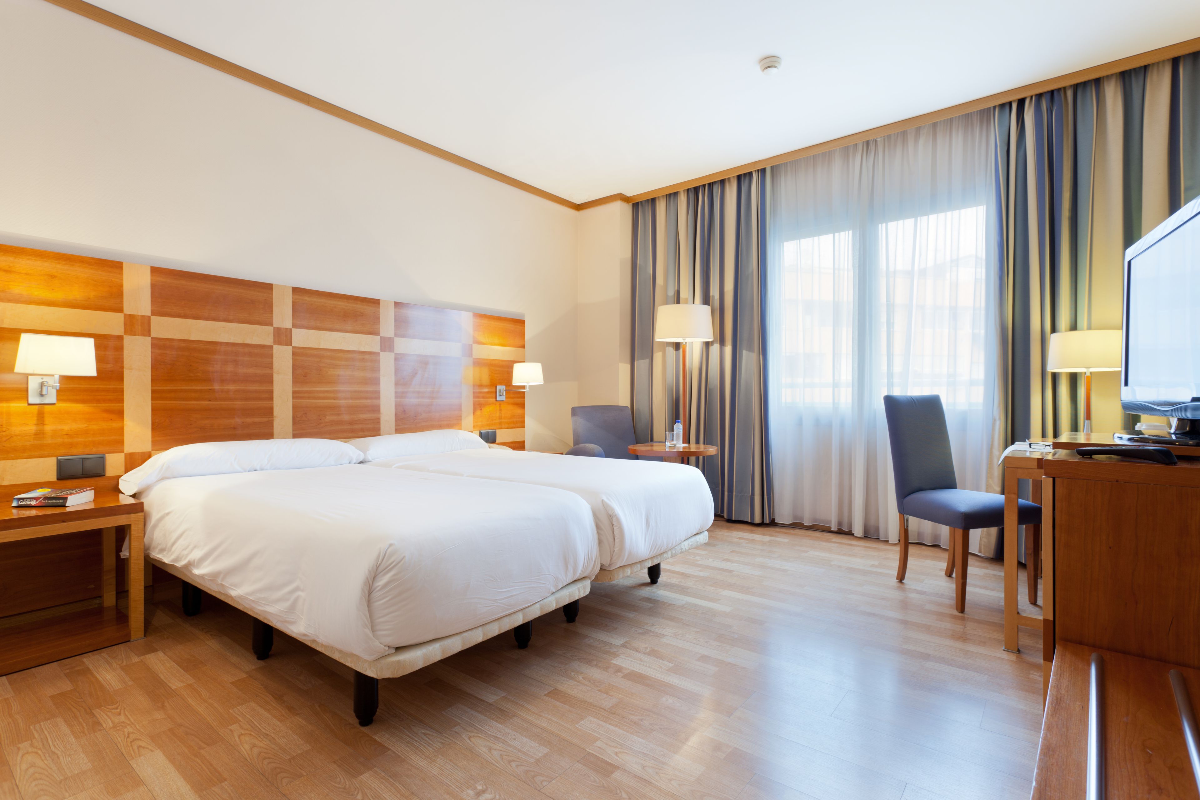 A hotel room with two beds, a desk, a chair, and a TV.