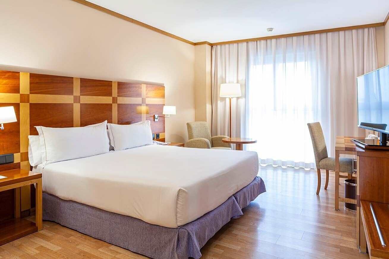 A hotel room with a large bed, a desk with a chair, a TV, and a window with curtains.
