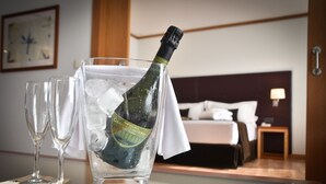 Eine Champagnerflasche in einem Glas mit Eiswürfeln, zwei leere Champagnerkelche und ein Bett im Hintergrund.