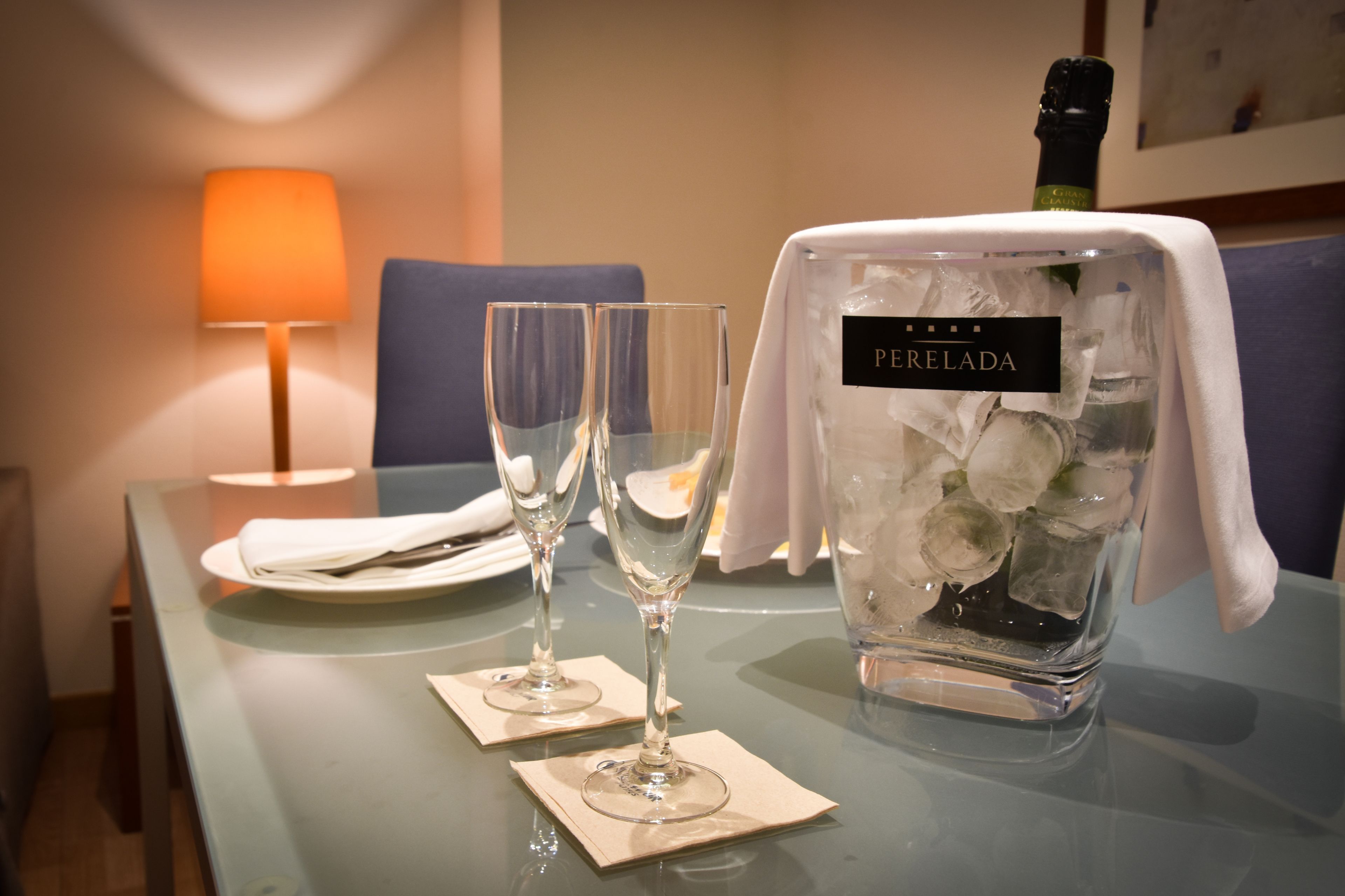 A table with two wine glasses, a bottle of champagne, and a bottle of Perelada wine.