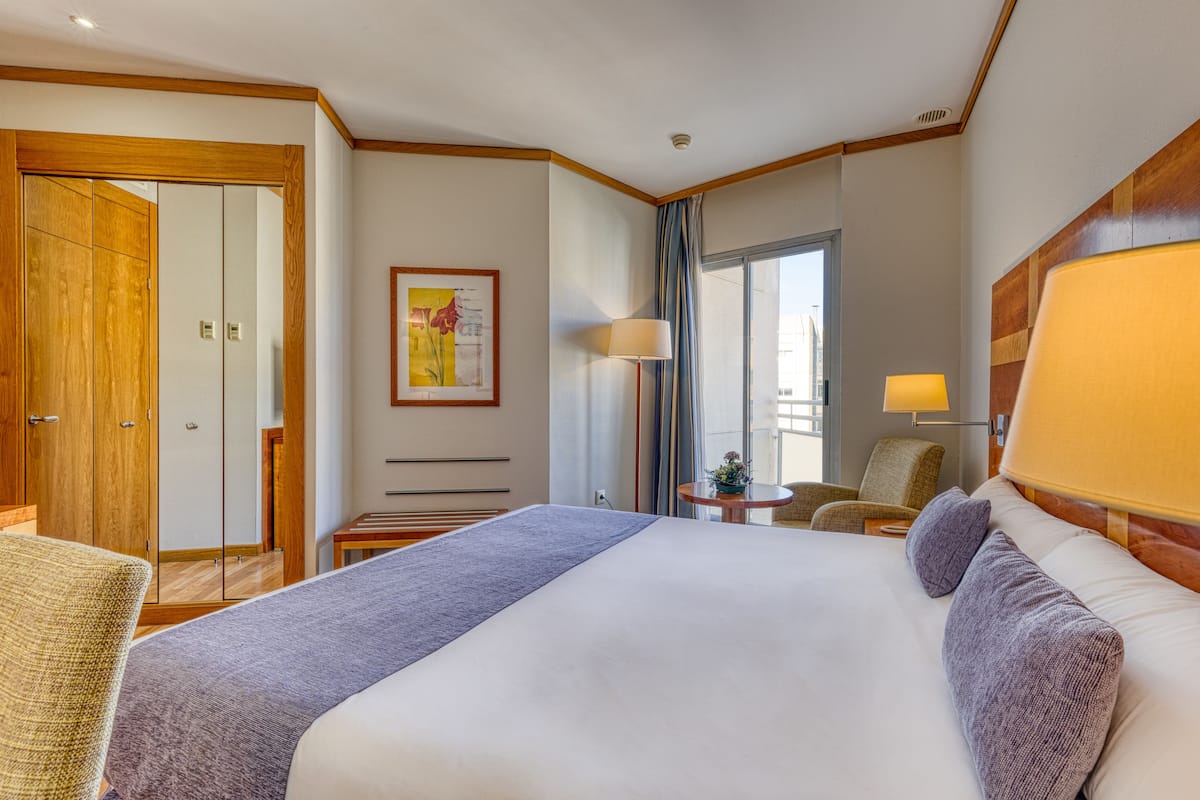 Une chambre d’hôtel avec un grand lit, une armoire en bois, une petite table avec une lampe et une chaise.