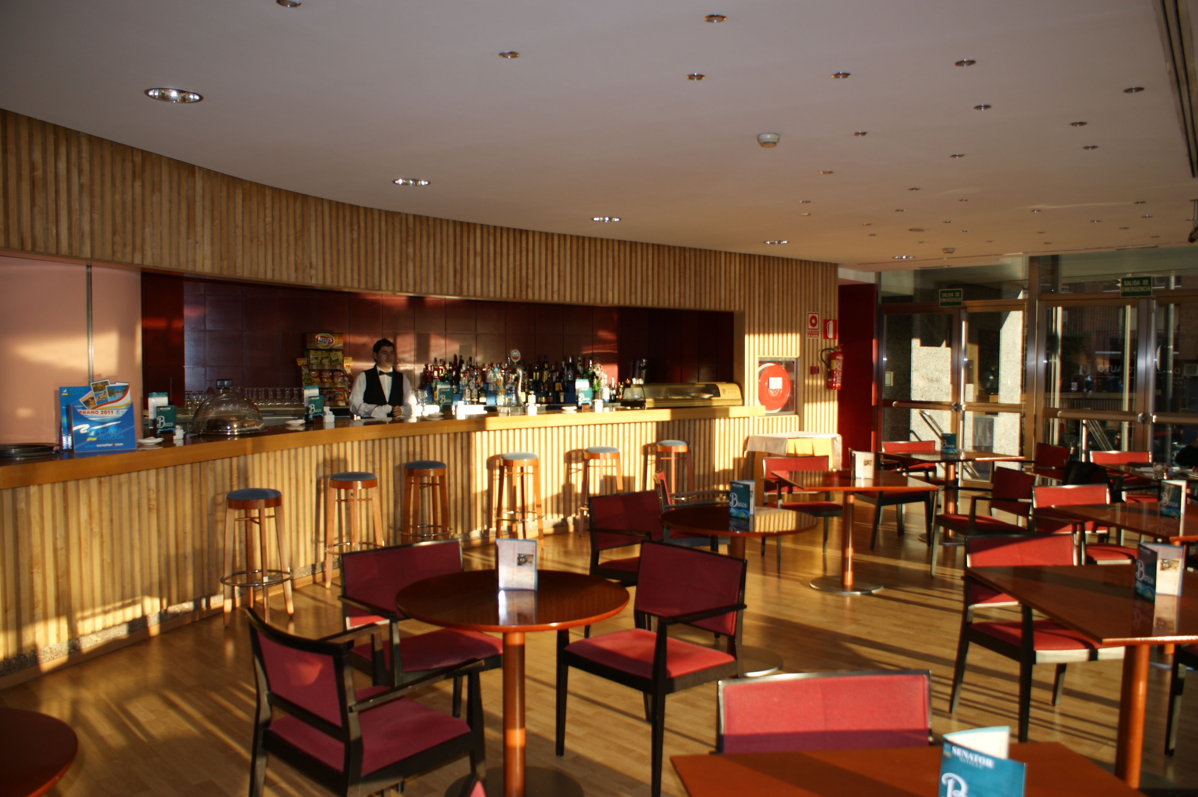 Un restaurante moderno con paneles de madera, una zona de bar y sillas y mesas rojas.