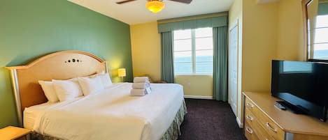 Une chambre d’hôtel comprenant un lit, une télévision, un ventilateur de plafond, une fenêtre donnant sur la mer et une commode.