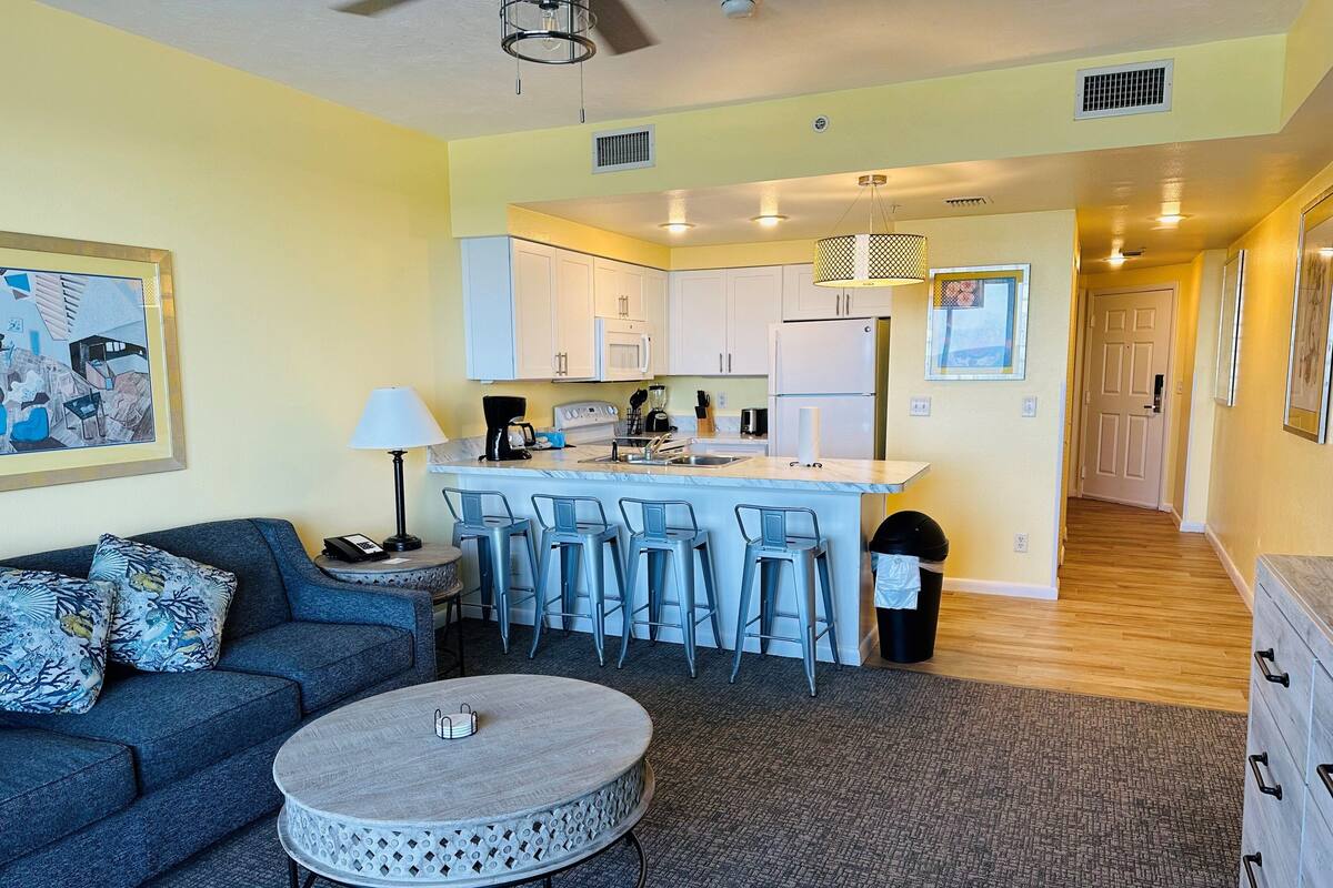 A compact living space with a sofa, a round coffee table, and a kitchen area featuring a refrigerator, stove, and bar stools.