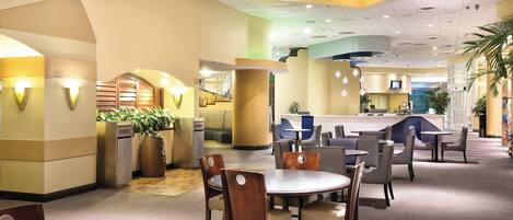 A hotel lobby with round tables and chairs, a reception desk, and a staircase leading to an upper level.