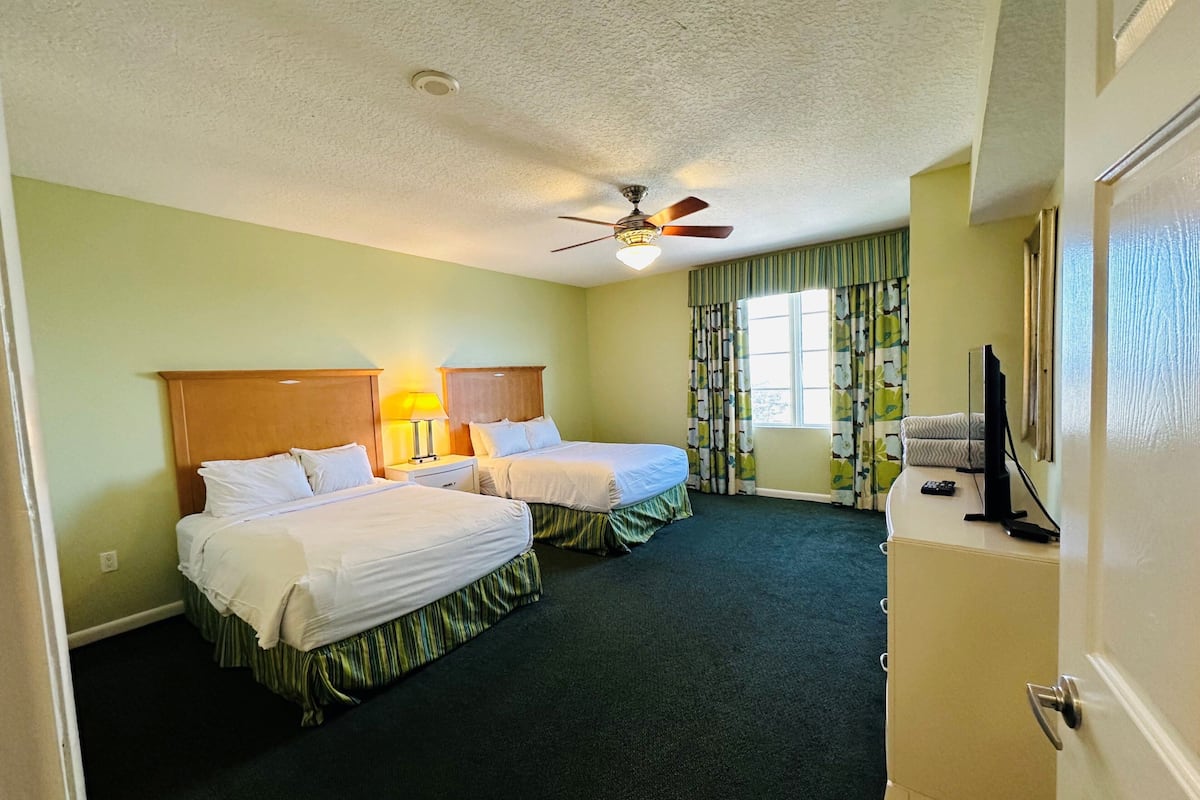 A hotel room with two beds, a ceiling fan, a TV, and a window with curtains.