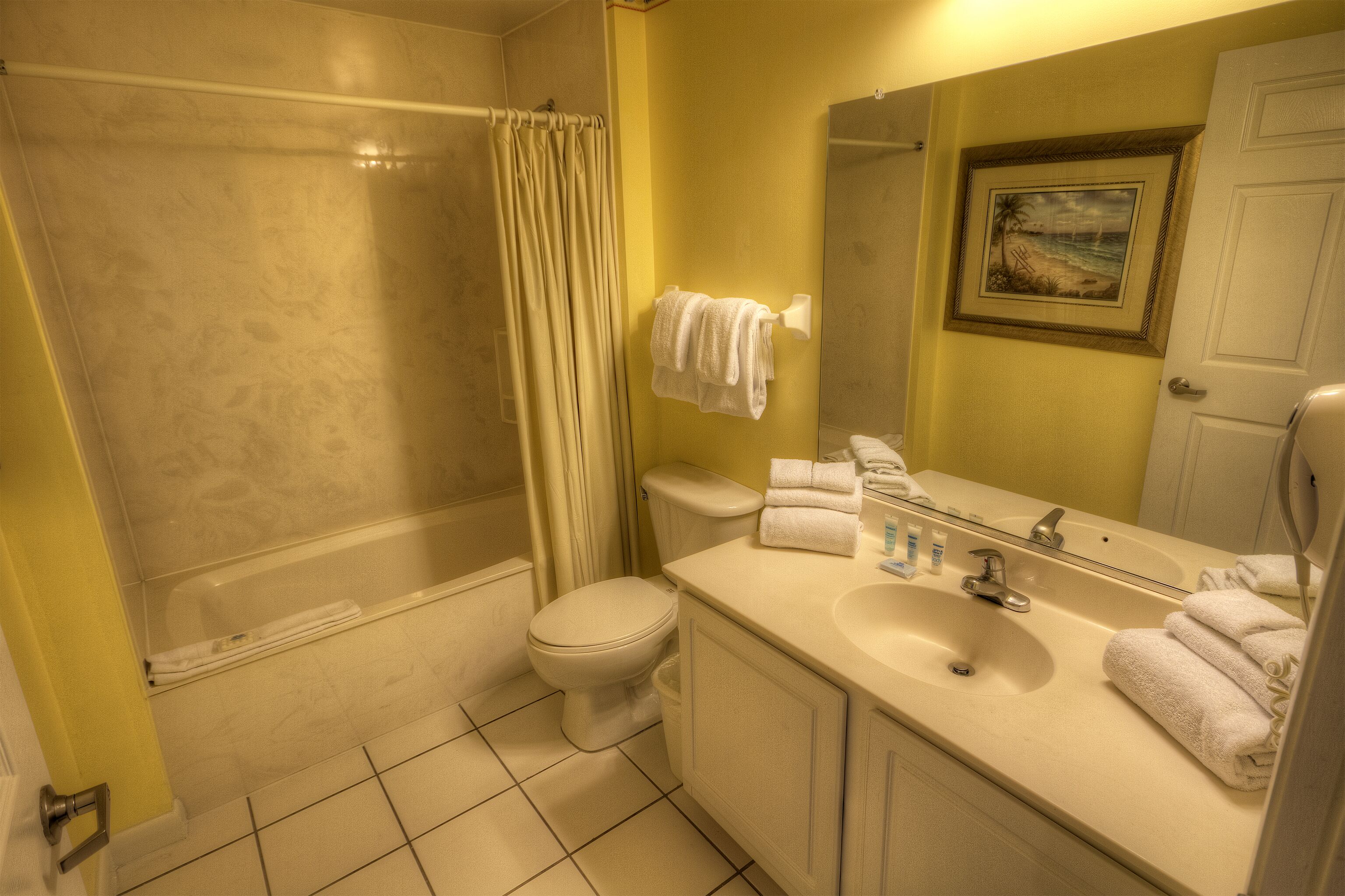 A bathroom with a bathtub, toilet, sink, and a framed picture on the wall.