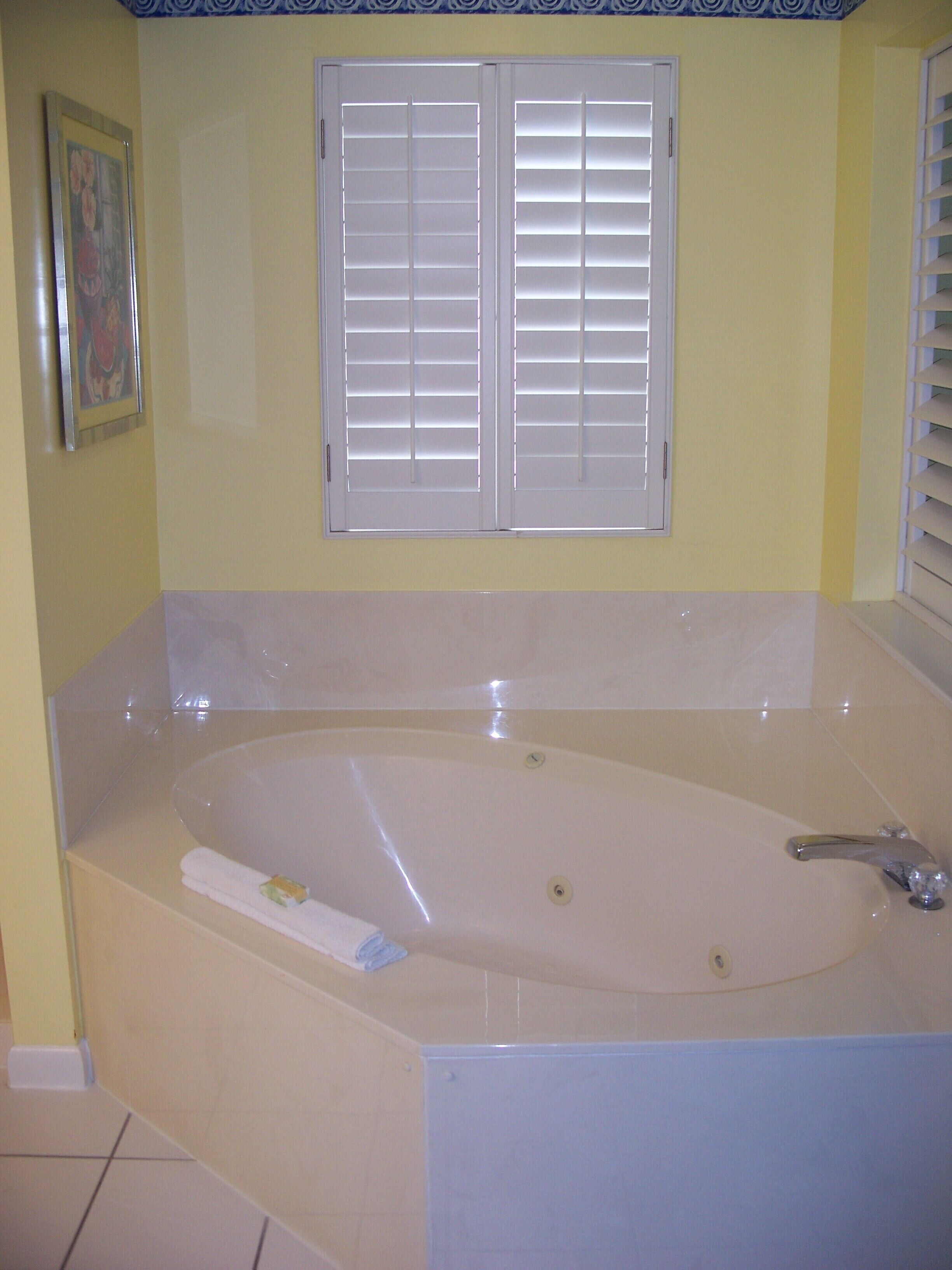 A bathroom with a large bathtub, a framed picture on the wall, and a window with blinds.
