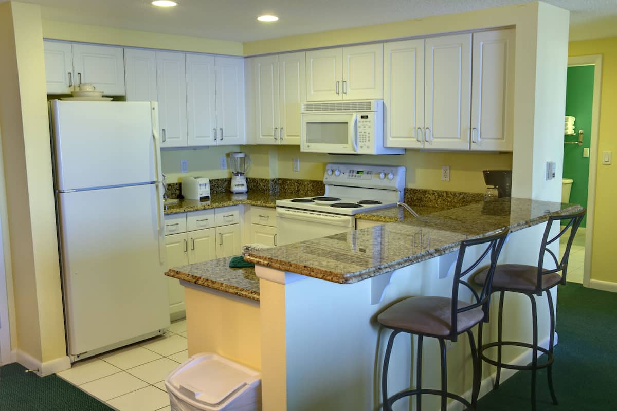 A kitchen with white cabinets, a refrigerator, a microwave, a stove, and a granite countertop.
