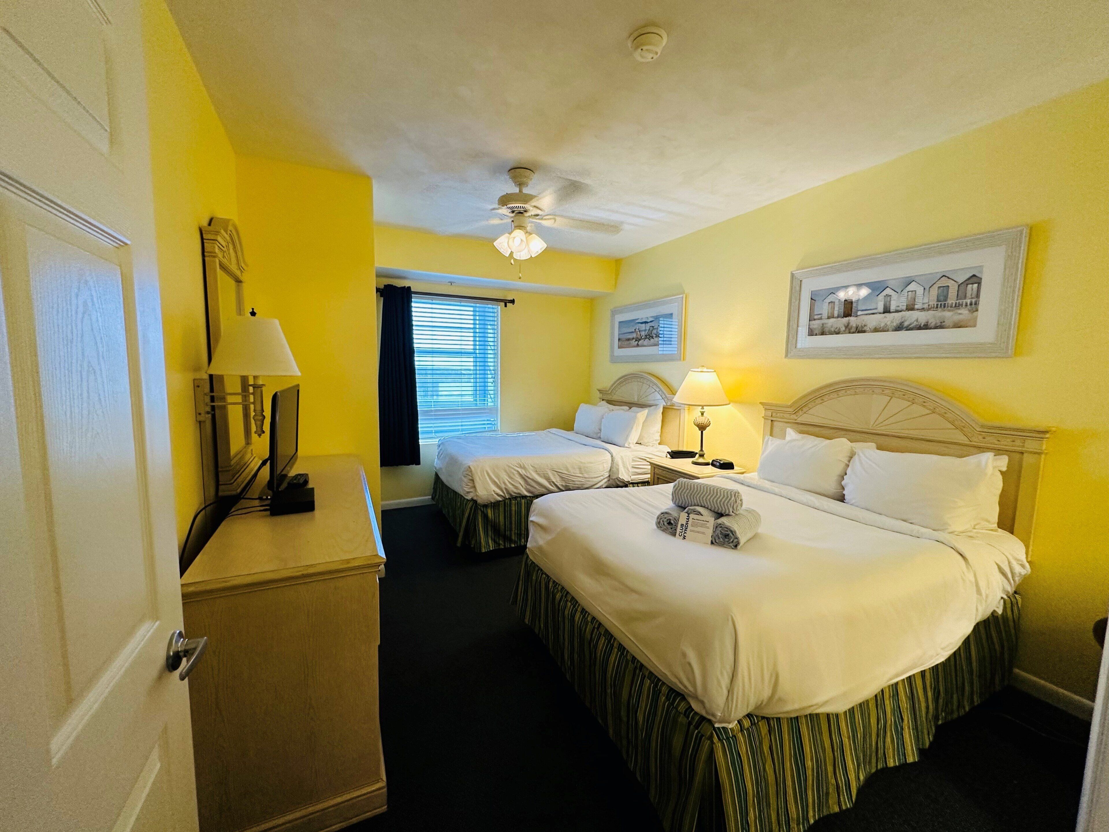 Une chambre d’hôtel avec deux lits, un bureau, une lampe et un ventilateur de plafond.