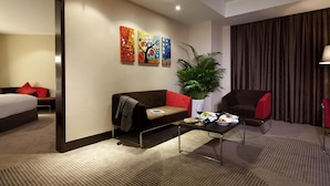 A hotel room with a bed, a sofa, a coffee table with a bottle and glasses, a plant, and three paintings on the wall. - Novotel Shenzhen Watergate (Shenzhen)