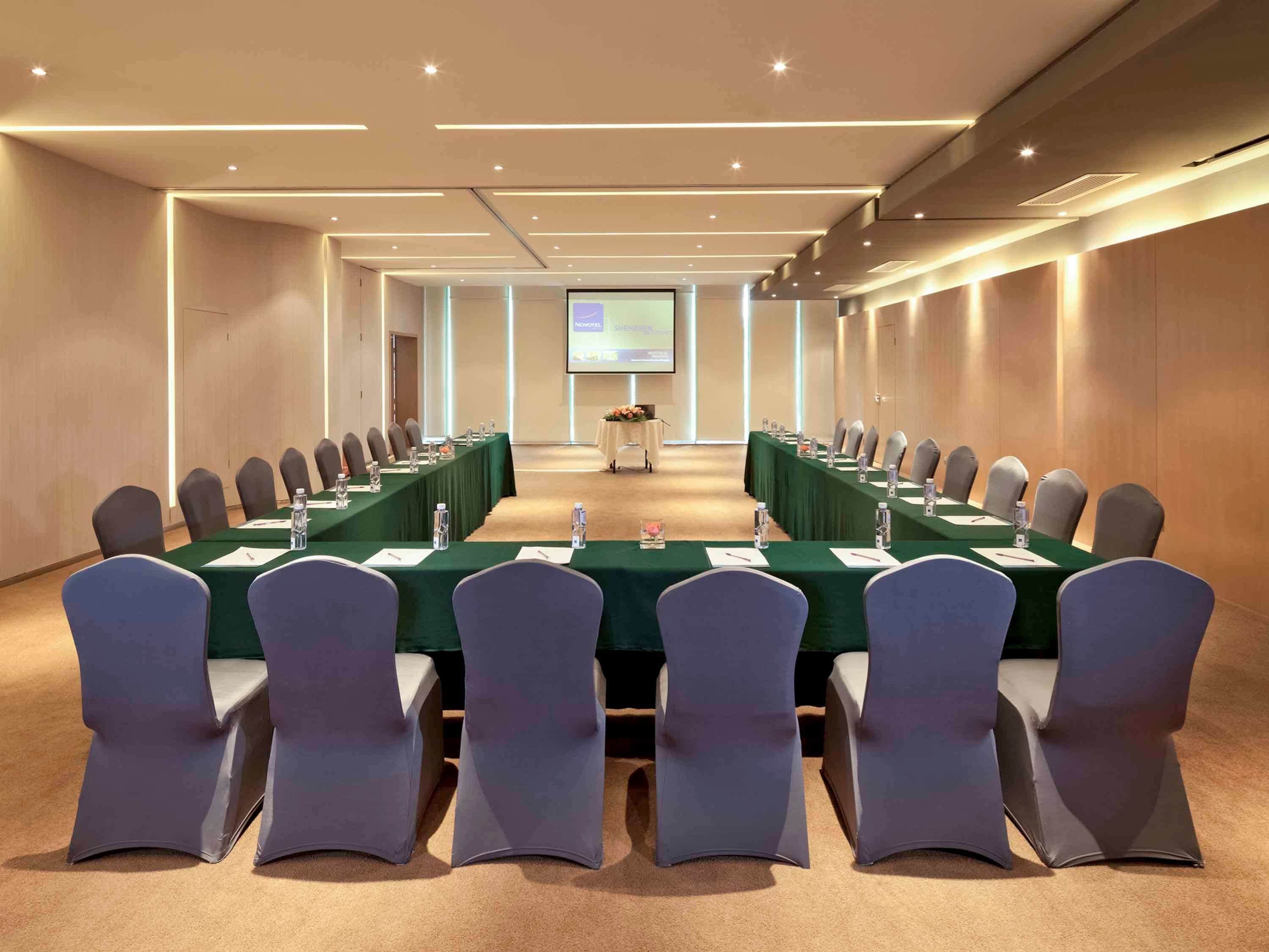 Une salle de conférence avec une longue table, des chaises et un écran de projection à l’avant.
