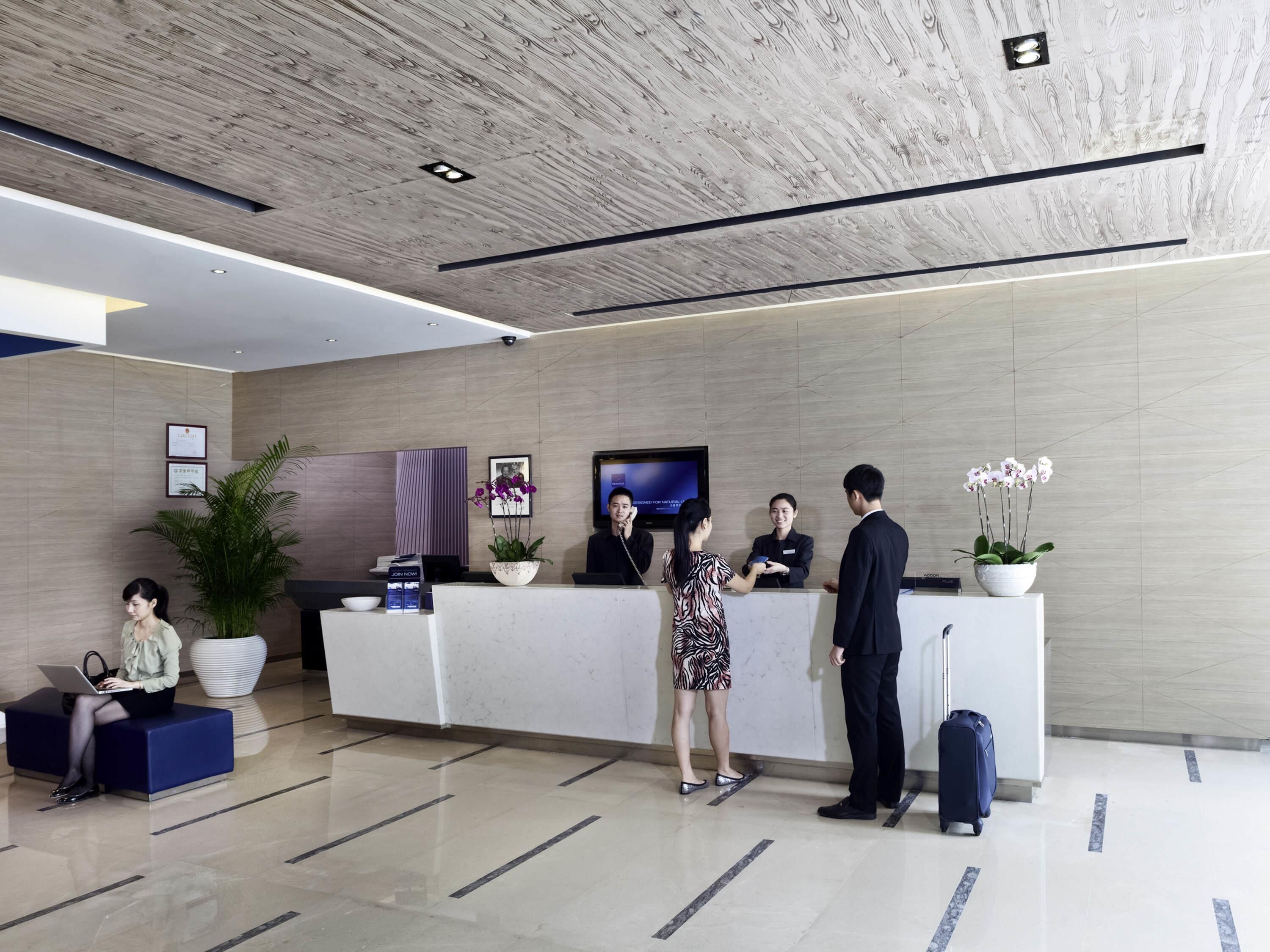 A modern reception area with a reception desk, a large potted plant, a flat-screen TV, and a seating area with a blue sofa.