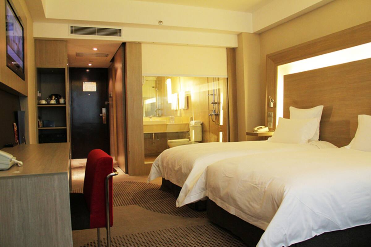 A hotel room with a bed, a desk, a chair, and a bathroom visible through an open door.