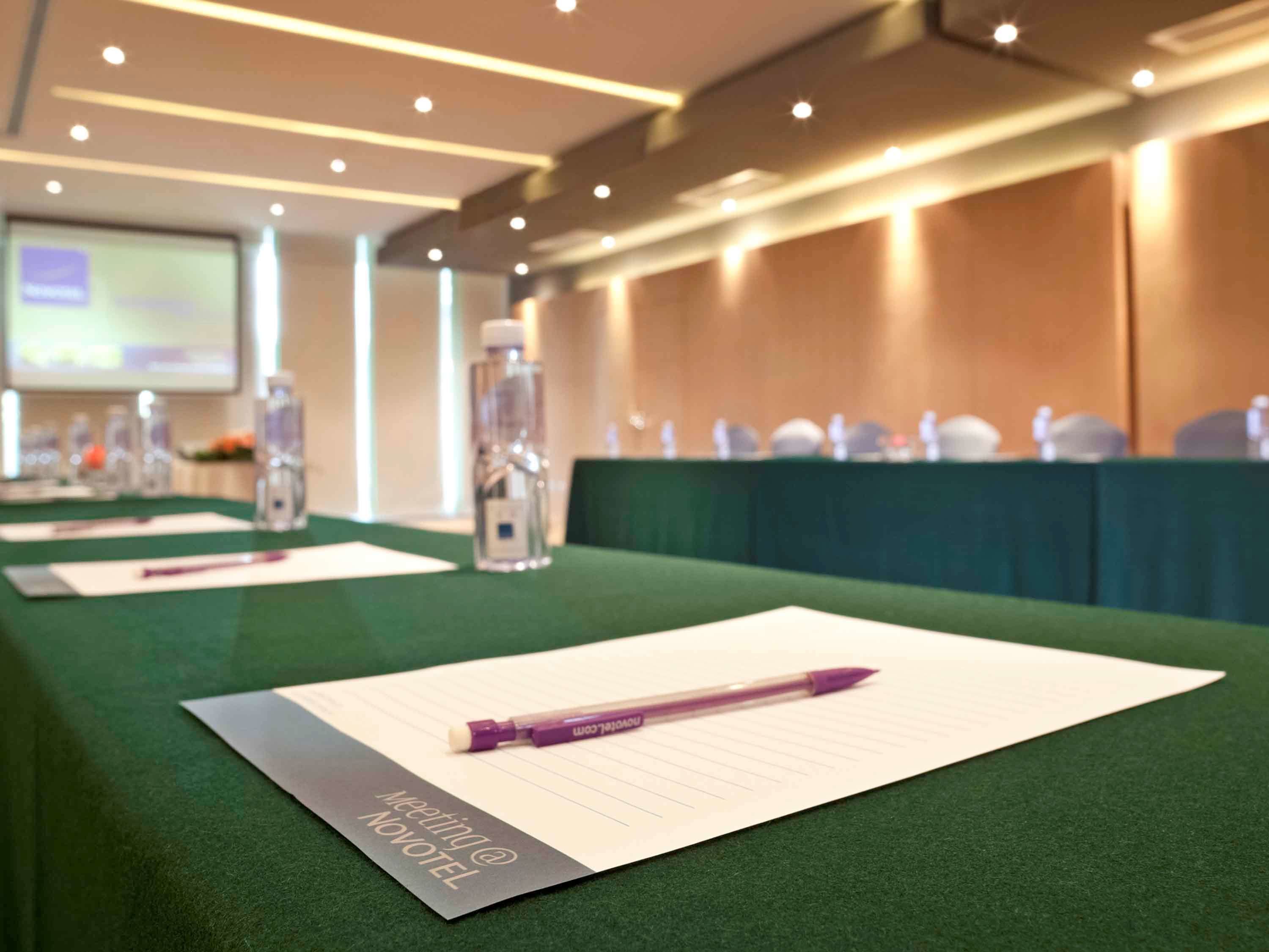 Une salle de conférence avec une longue table, des bouteilles d’eau et des stylos posés sur une nappe verte.