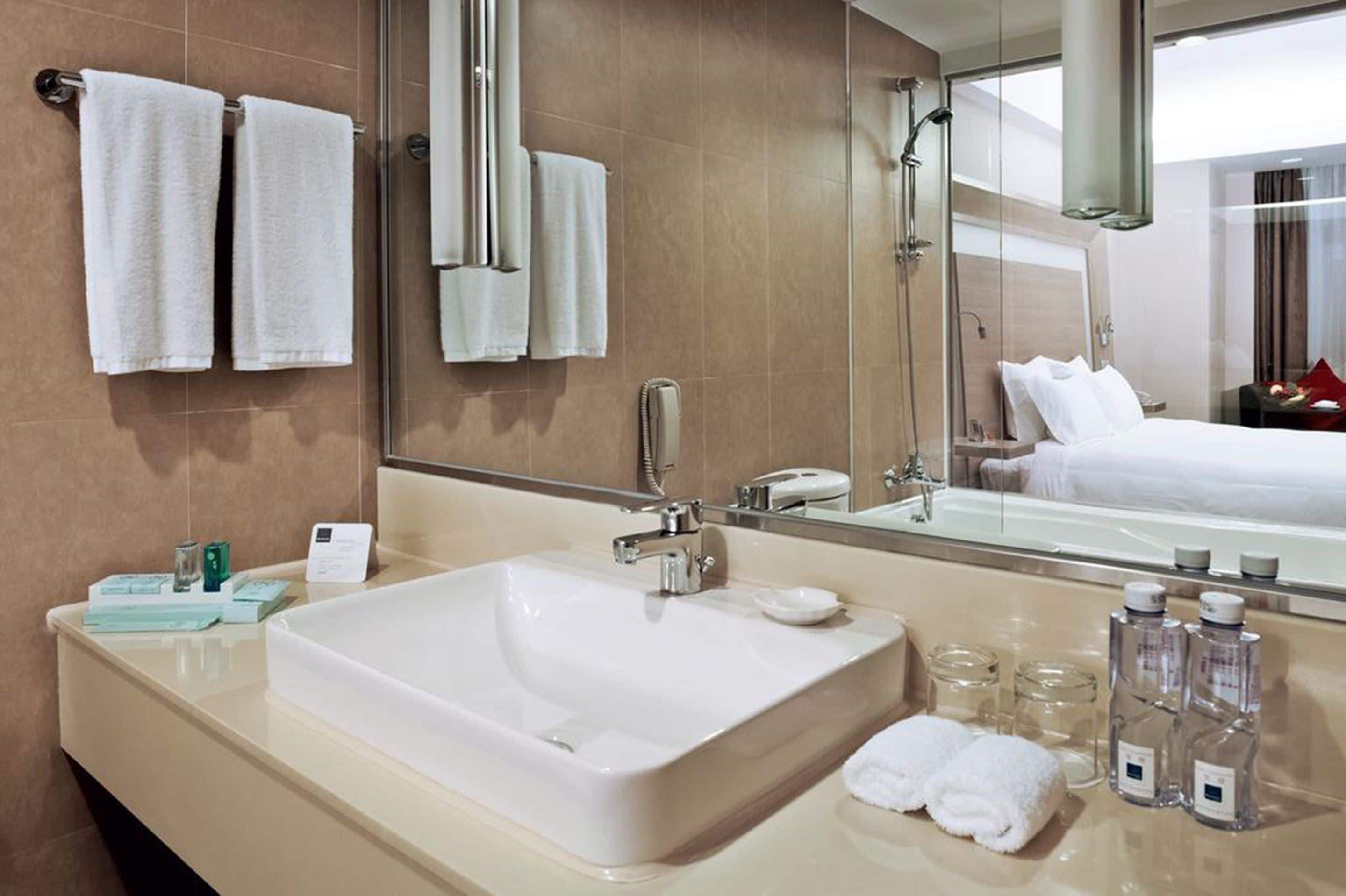 A hotel bathroom with a large sink, a mirror, and a shower.