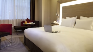 A hotel room with a large bed, a desk with a laptop, a chair, and a small table with a tray of breakfast items. - Novotel Shenzhen Watergate (Shenzhen)