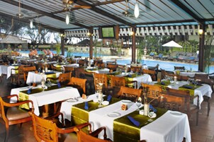Un restaurante al aire libre con mesas dispuestas para comer, una zona de piscina con sillones de descanso y un área de estar cubierta.