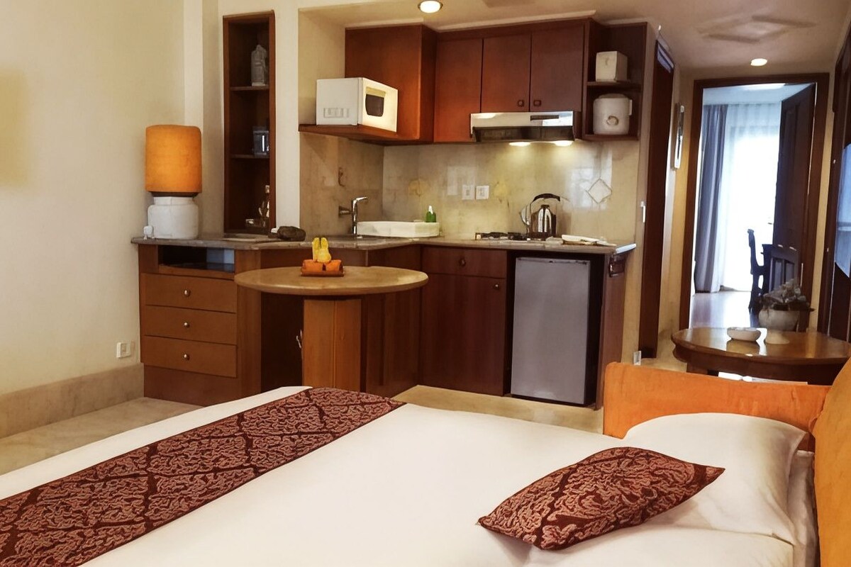A compact hotel room with a bed, a small kitchenette, a bathroom, and a view of the outside.