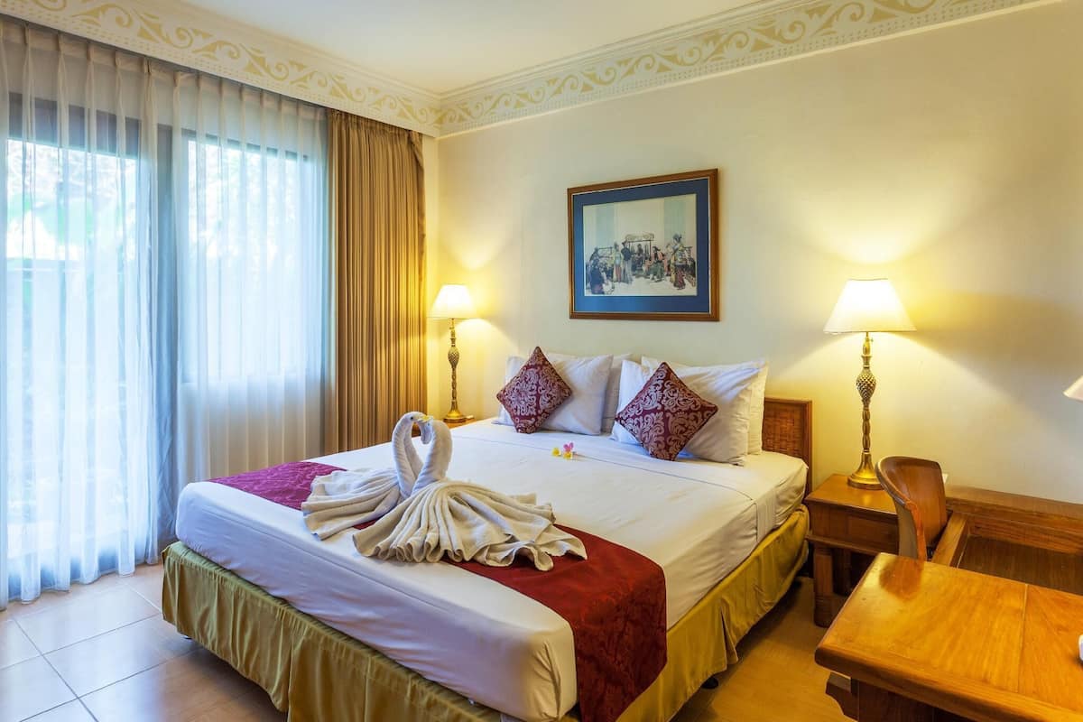 Habitación de hotel con una cama bien hecha, dos lámparas de noche, un cuadro en la pared y una ventana con cortinas.
