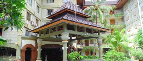A traditional building with a central pavilion, surrounded by lush greenery and a small water feature.