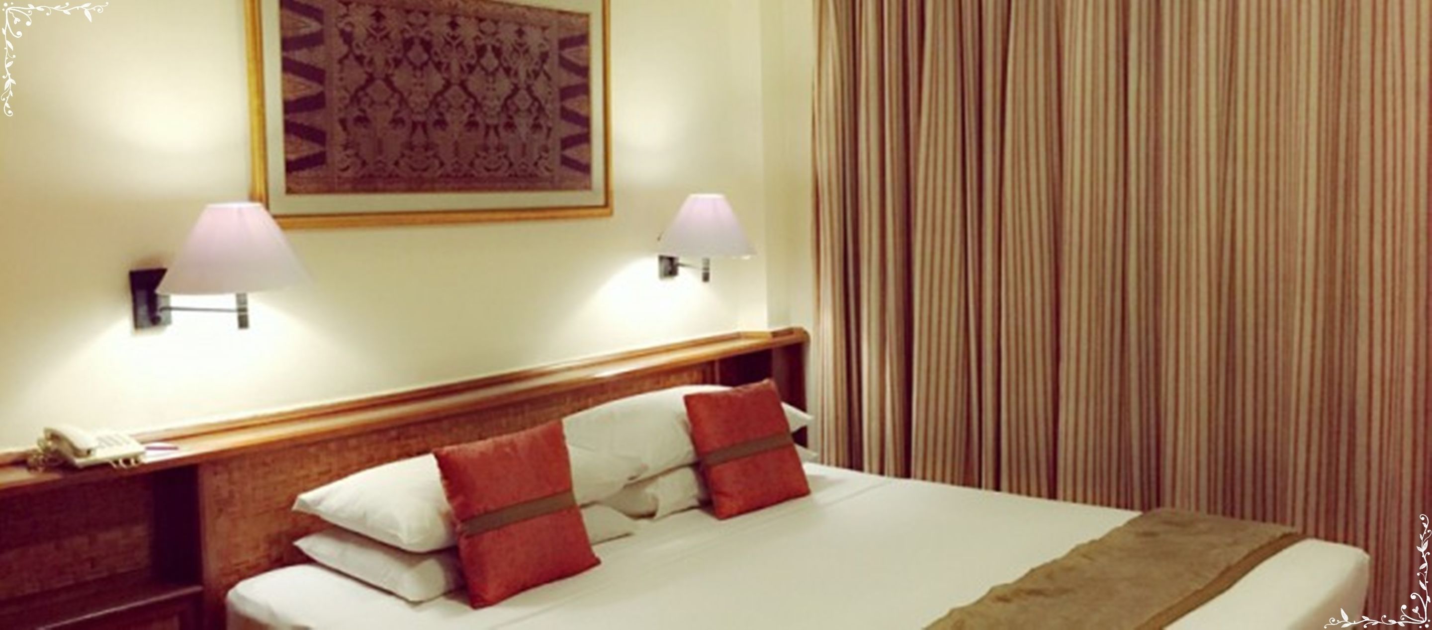 A hotel room with a bed, two bedside lamps, a telephone, and a patterned wall hanging.